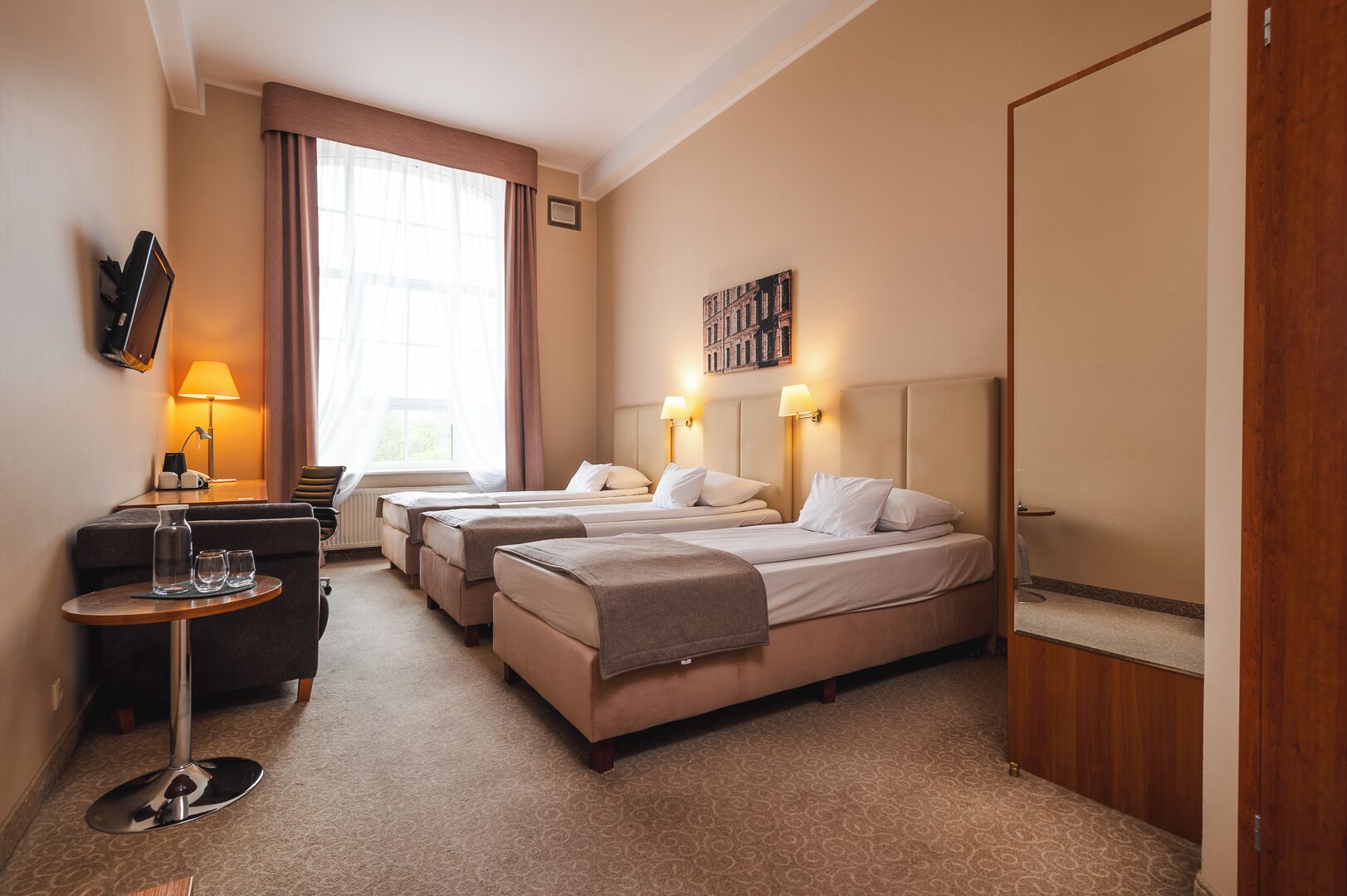 Een hotelkamer met twee bedden, een bureau met een lamp, een televisie en een raam met gordijnen.