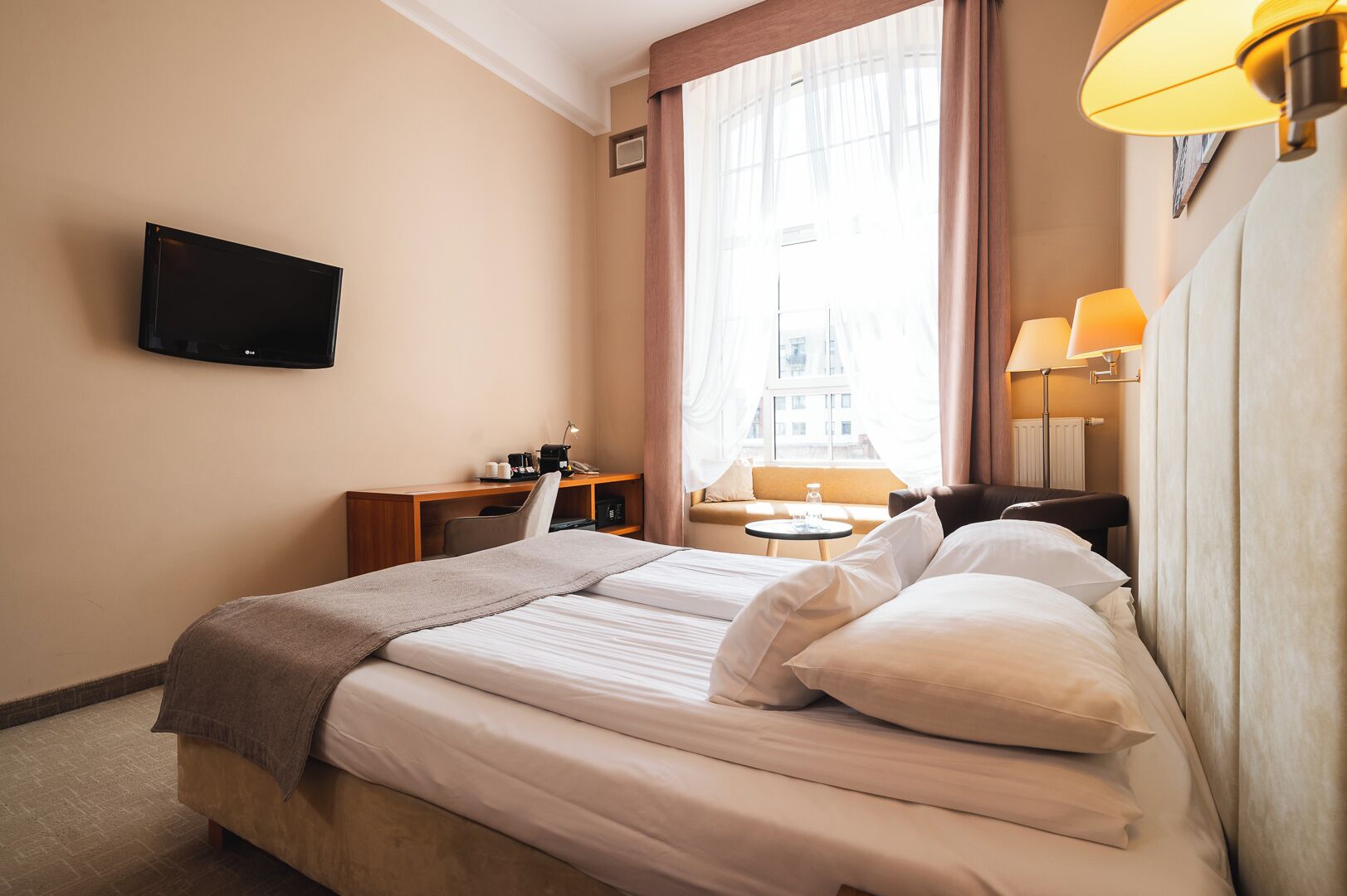 Habitació d'hotel amb llit, escriptori, cadira, televisió i finestra amb cortines.