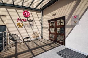 A hotel entrance with a glass door, a signboard with the hotel's logo, and two wicker chairs outside. - Hotel Focus Lodz (Lodz)