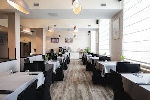 A restaurant with multiple tables, black chairs, and a wooden floor. - Hotel Focus Lodz (Lodz)