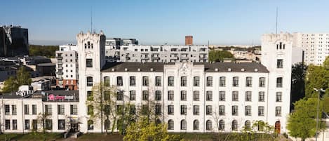 Ein großes, weißes Gebäude mit zahlreichen Fenstern und einem zentralen Turm, umgeben von Bäumen und weiteren Gebäuden.