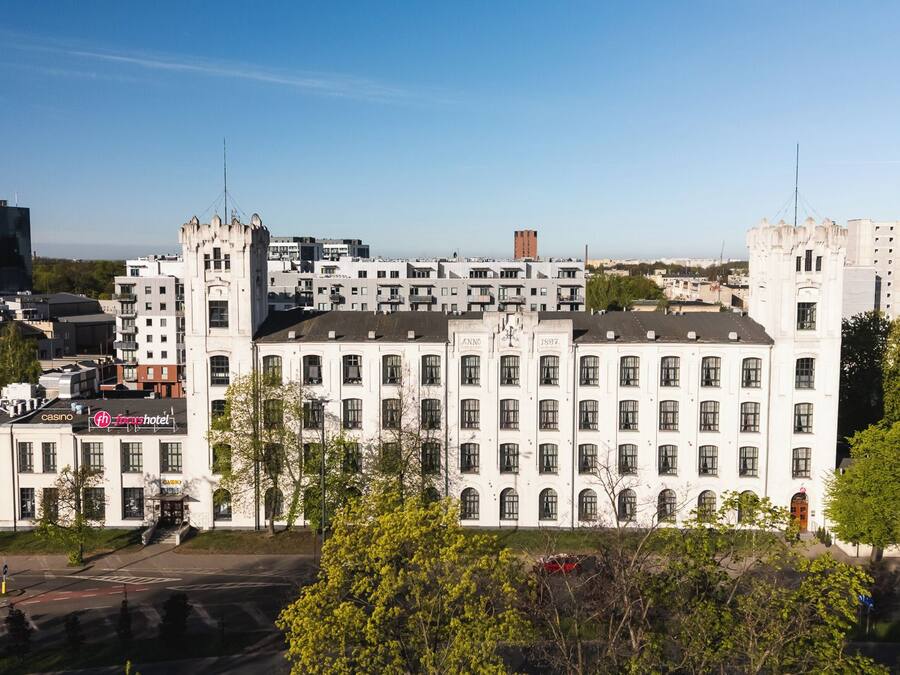 En stor vit byggnad med många fönster och ett centralt torn, omgiven av träd och andra byggnader.