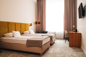 A hotel room with two beds, a desk, a chair, a TV, and a window with curtains.