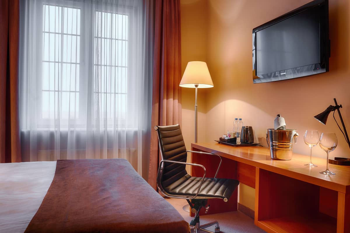 Een hotelkamer met een bed, een bureau met lamp, een stoel, een televisie en een raam met gordijnen.