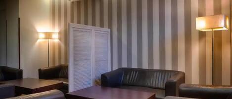 Um quarto com papel de parede listrado, um sofá, duas poltronas, uma mesa de centro e duas luminárias de chão.