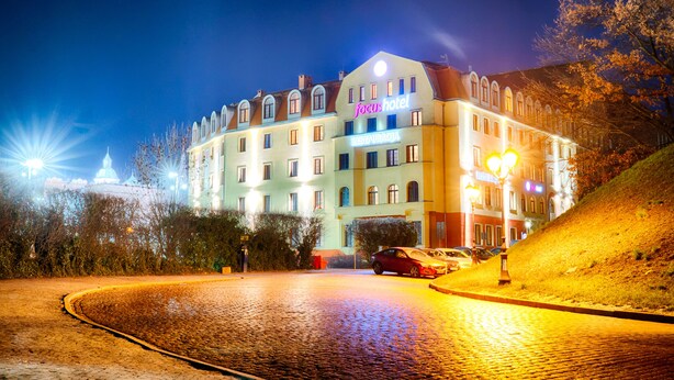 Un hôtel avec une enseigne indiquant « focus hotel » et « RESTAURACJA », ce qui signifie qu’il y a un restaurant au rez-de-chaussée.