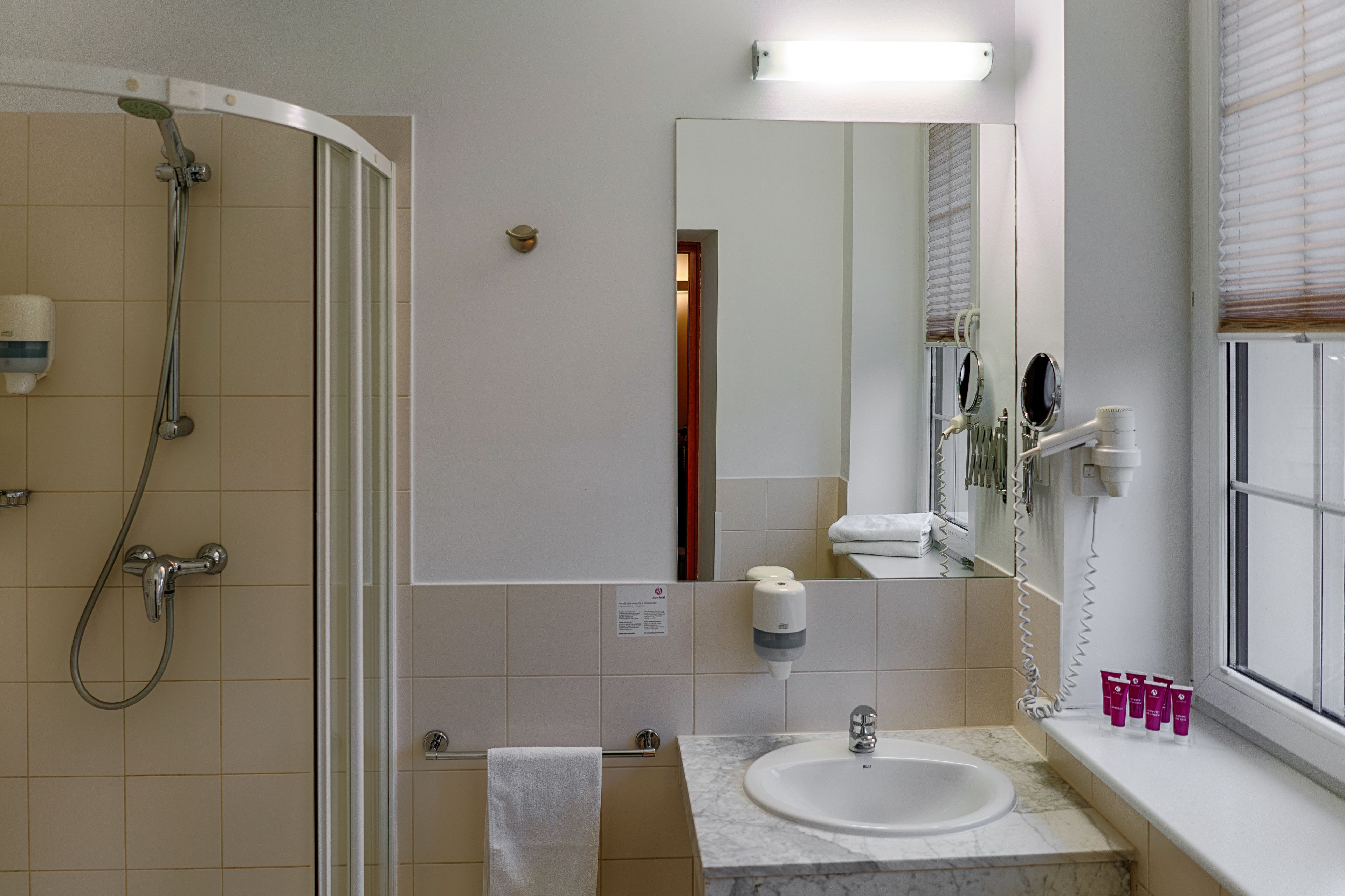 A bathroom with a shower, sink, mirror, and toiletries.