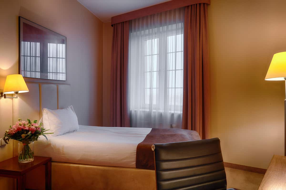 Een hotelkamer met een bed, een stoel, een bureau met een lamp en een raam met gordijnen.