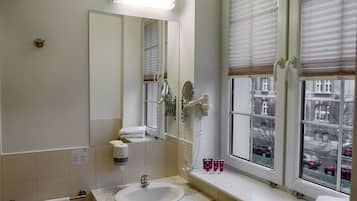 Een badkamer met een wastafel, spiegel, handdoekrek en raam met zonwering.