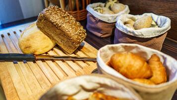 A wooden cutting board with a loaf of bread, a knife, and a basket of pastries.