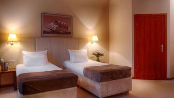 A hotel room with two beds, a wooden door, and a framed picture on the wall.