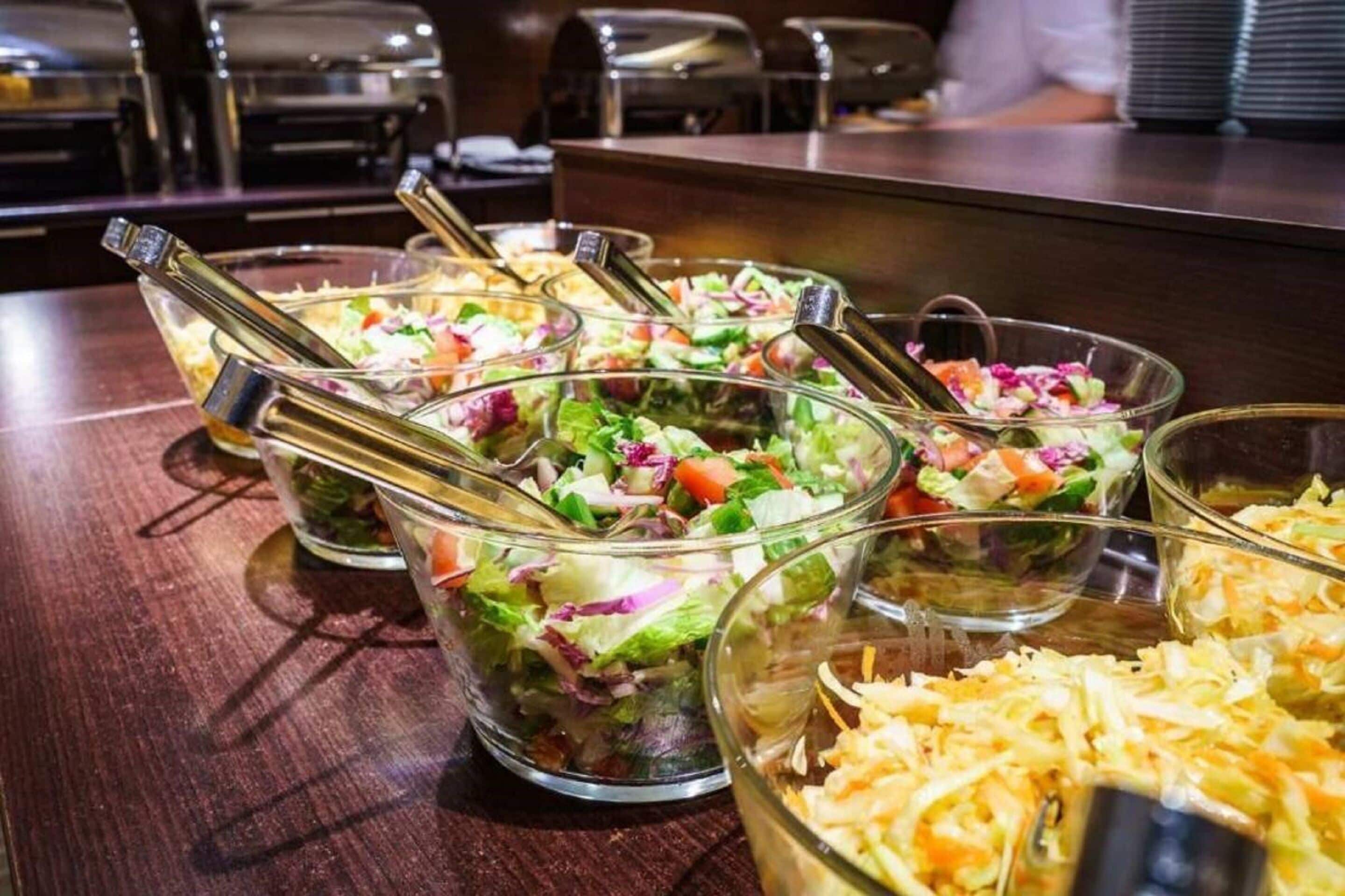 Une table de buffet proposant diverses salades et du fromage râpé.