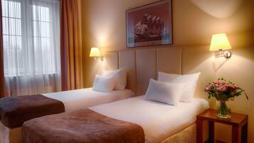 A hotel room with two beds, a nightstand with a lamp, a framed picture on the wall, and a window with curtains.