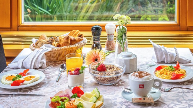 A breakfast table with various dishes, a basket of bread, a salt and pepper set, a flower vase, and a window view. - Corvin Hotel Budapest - Corvin wing (Budapest)