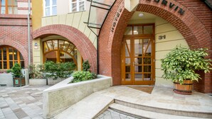 A building entrance with a brick facade, a large arched doorway, and a potted plant. - Corvin Hotel Budapest - Corvin wing (Budapest)
