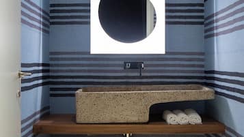 Un baño pequeño con paredes a rayas, un espejo redondo, un lavabo con encimera y una cesta de mimbre.