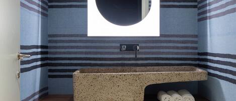 A small bathroom with striped walls, a round mirror, a countertop sink, and a wicker basket.