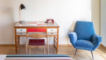 Um quarto com uma escrivaninha de madeira, um telefone vermelho, uma cadeira azul e um tapete listrado.