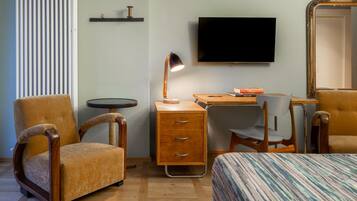 A room with a bed, two armchairs, a desk with a lamp, a television, and a mirror.