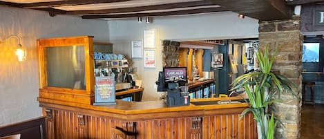 Una zona de bar con mostrador de madera, una pantalla de televisión y un cartel que promociona Cask Ales.