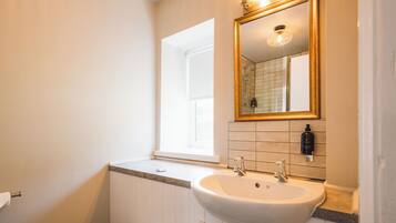 Un baño con un lavabo blanco, un espejo con marco dorado y una ventana.