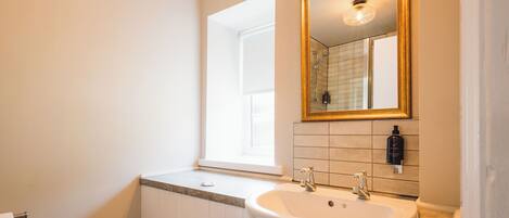 A bathroom with a white sink, a mirror with a gold frame, and a window.