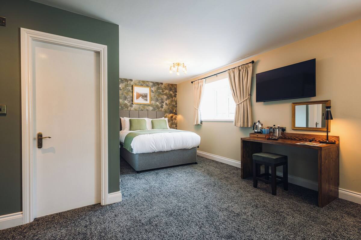 A bedroom with a bed, a desk, a chair, a television, and a window with curtains.