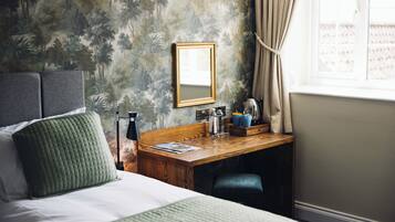 Une chambre d’hôtel avec un lit, un bureau doté d’un miroir, une fenêtre avec des rideaux et un mur orné d’un motif représentant une forêt.
