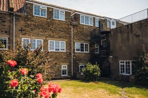 A stone building with multiple windows, a spiral staircase, and a small garden area with flowers.
