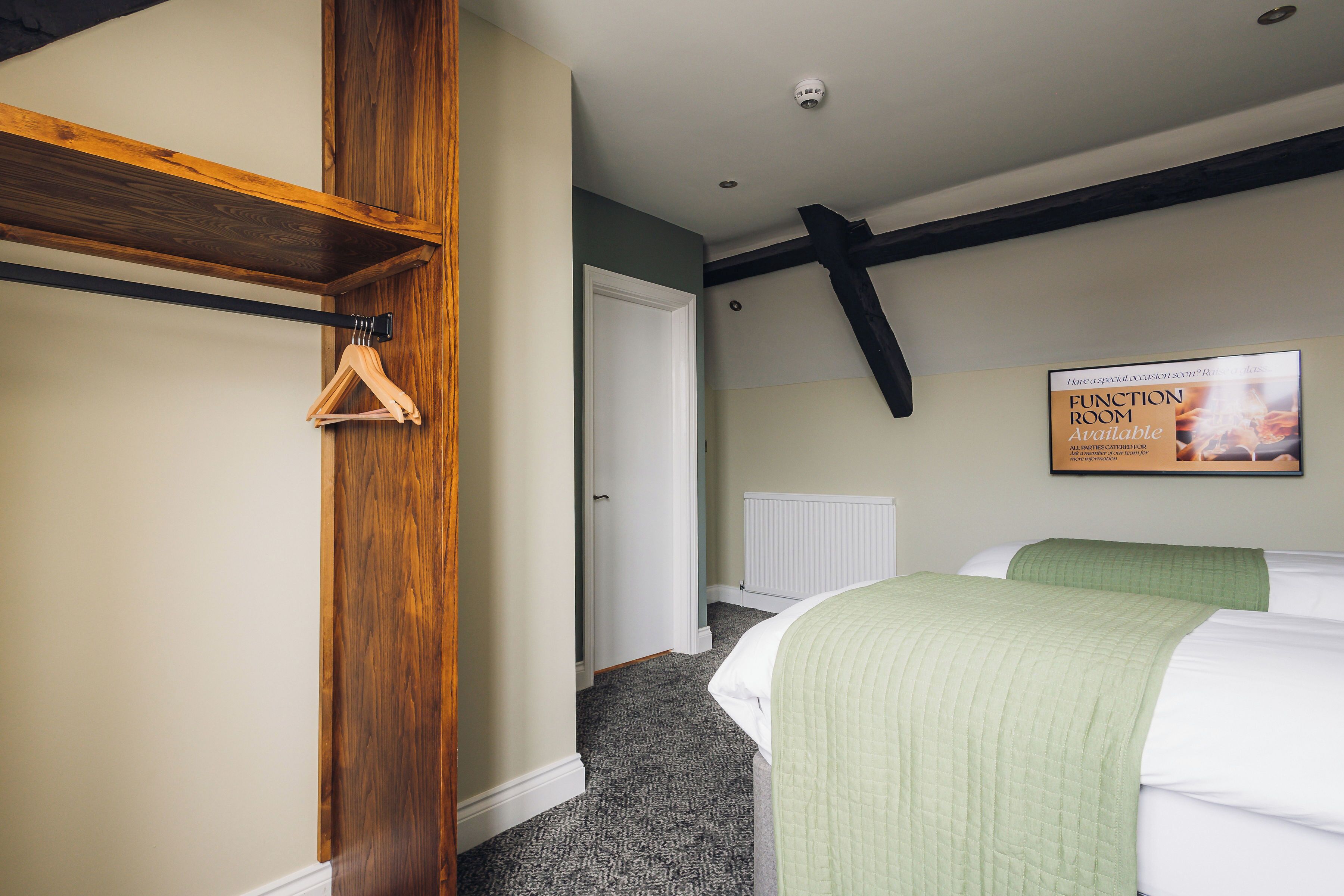 Une chambre avec un lit, une étagère en bois, un radiateur et un panneau indiquant qu’une salle polyvalente est disponible.