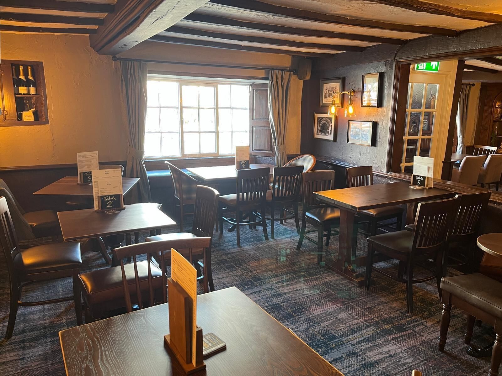 A restaurant interior with wooden tables and chairs, a menu stand, and framed pictures on the walls.
