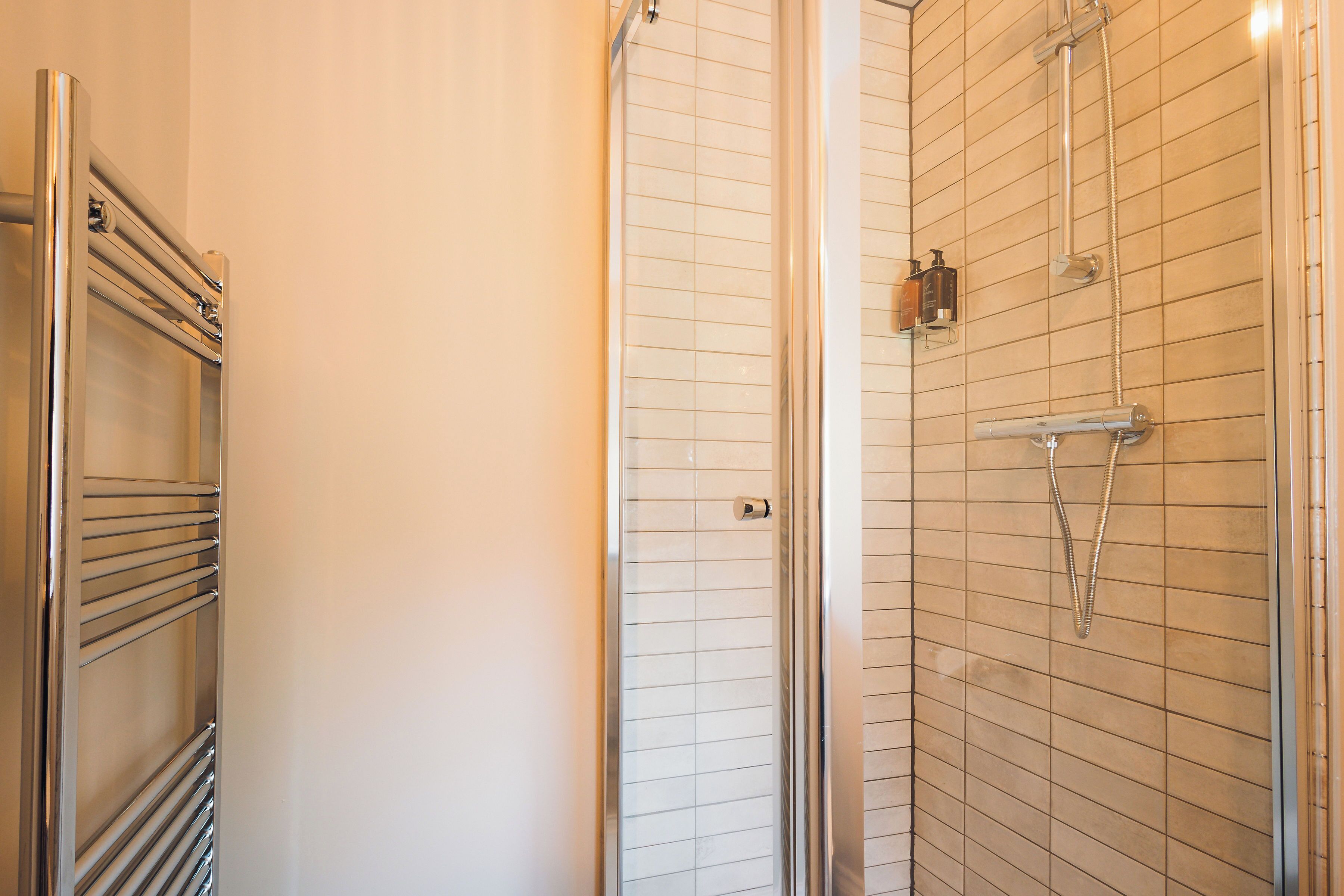 A bathroom with a glass shower enclosure, a chrome towel rack, and a tiled wall.