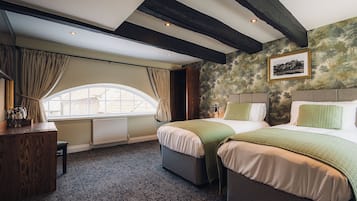 A hotel room with two beds, a desk, a window with curtains, and a fireplace.