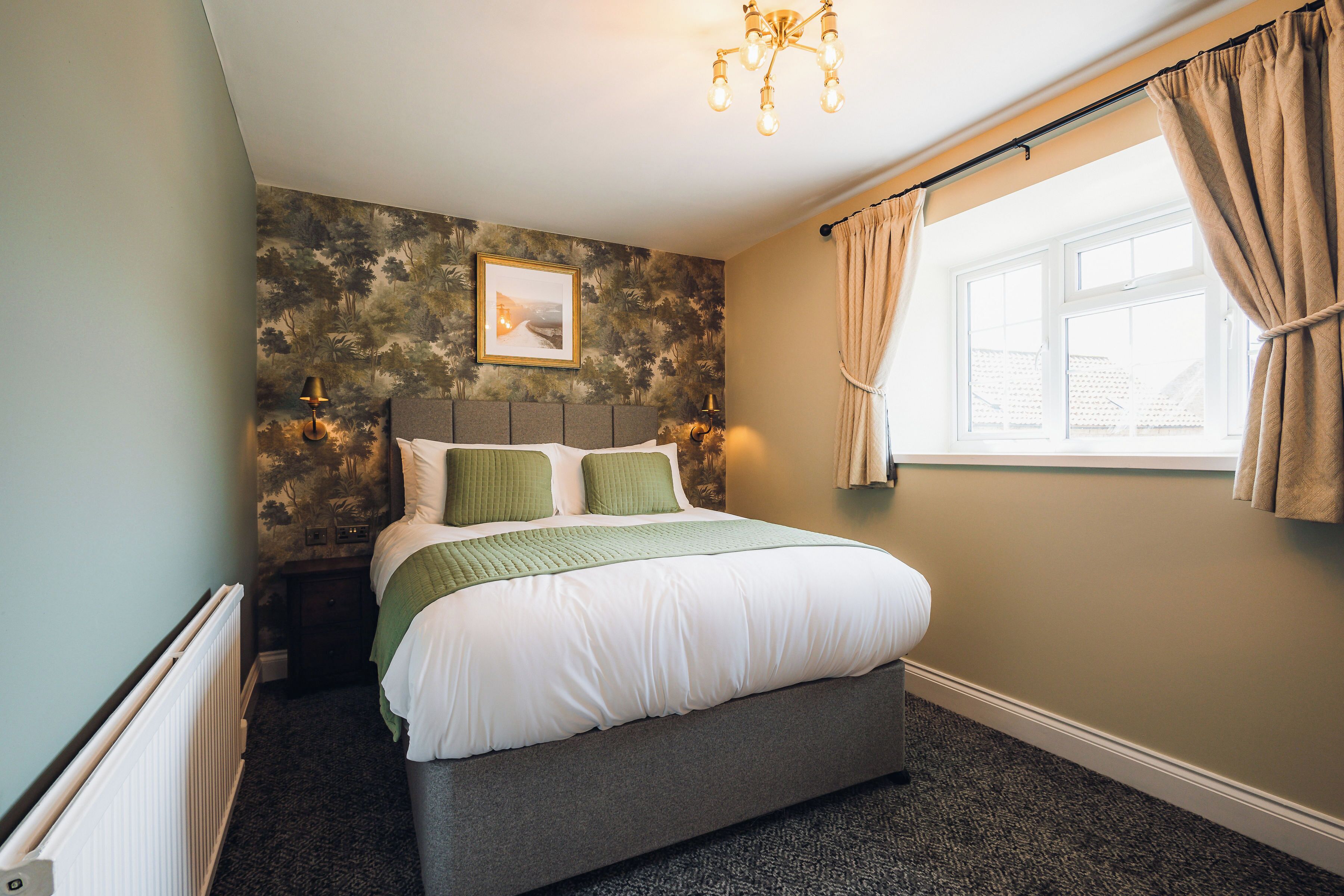 A bedroom with a bed, a window with curtains, a wall-mounted picture, and a radiator.