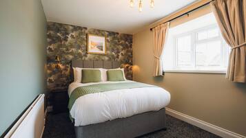 A bedroom with a bed, a window with curtains, a wall-mounted picture, and a radiator.