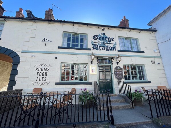 A building named 'The George Dragon' with a sign indicating it offers rooms, food, and ales.