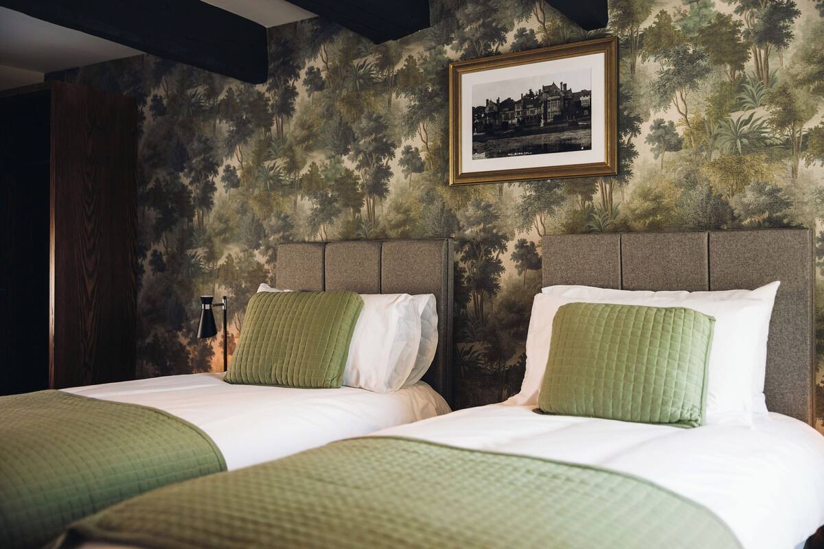 A bedroom with two beds, a framed picture on the wall, and a patterned wallpaper.