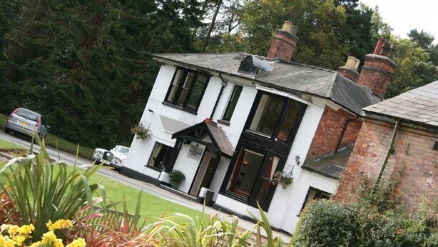 A two-story building with a white facade and black-framed windows, surrounded by a well-maintained garden with yellow and pink flowers. - Old Rose and Crown Hotel (Birmingham)