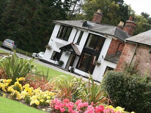 A two-story building with a white facade and black-framed windows, surrounded by a well-maintained garden with yellow and pink flowers. - Old Rose and Crown Hotel (Birmingham)