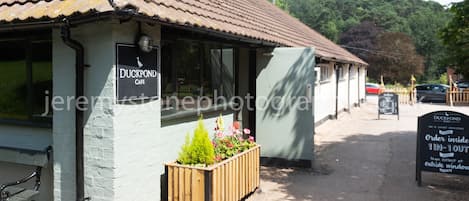 A Duckpond Cafe with a tiled roof, a wooden planter with flowers, and a sign indicating ordering inside.