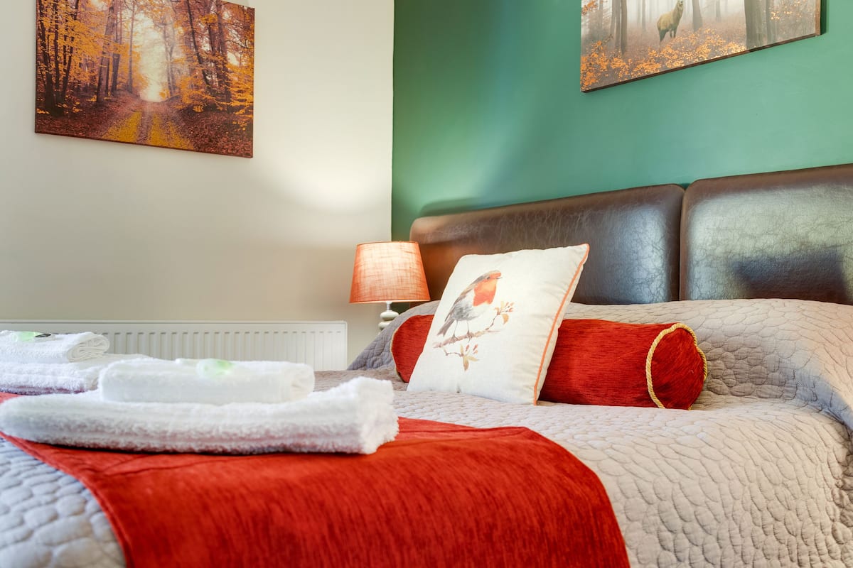 A neatly made bed with a red and white quilt, a pillow with a bird design, and a lamp on a bedside table.