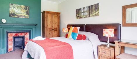 A bedroom with a bed, a nightstand, a wooden cabinet, a fireplace, and two wall-mounted paintings.