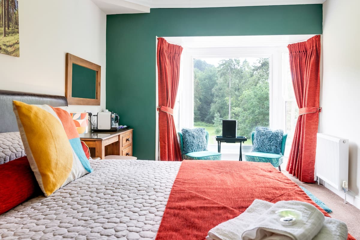 A bedroom with a bed, a desk, a chair, and a view of the outdoors.