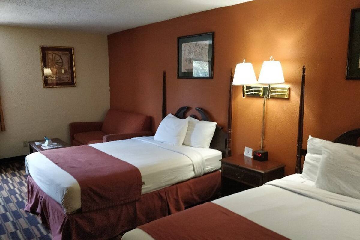A hotel room with two beds, a desk, and a nightstand. There is a framed picture on the wall and a lamp on the nightstand.
