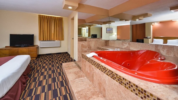 Una habitación de hotel con una cama grande, un jacuzzi rojo, un televisor y un espejo.