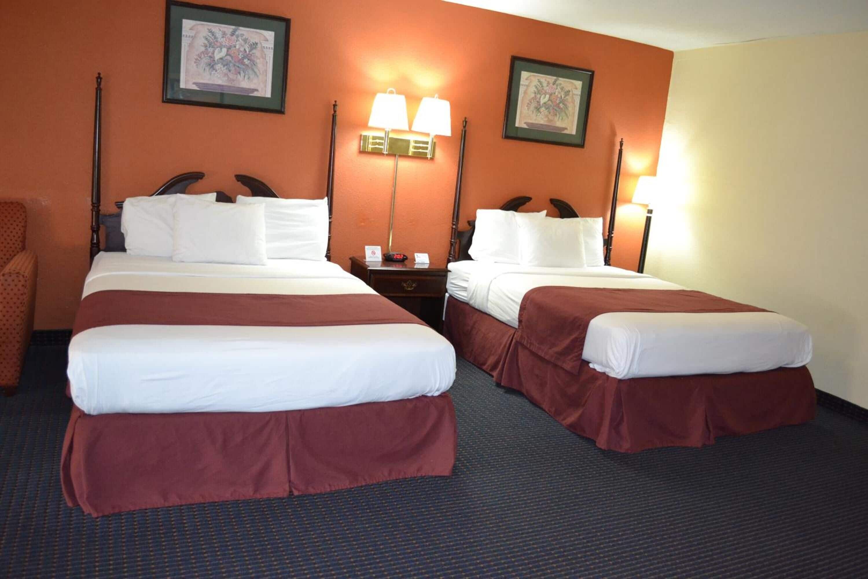 A hotel room with two beds, a nightstand, and a chair.