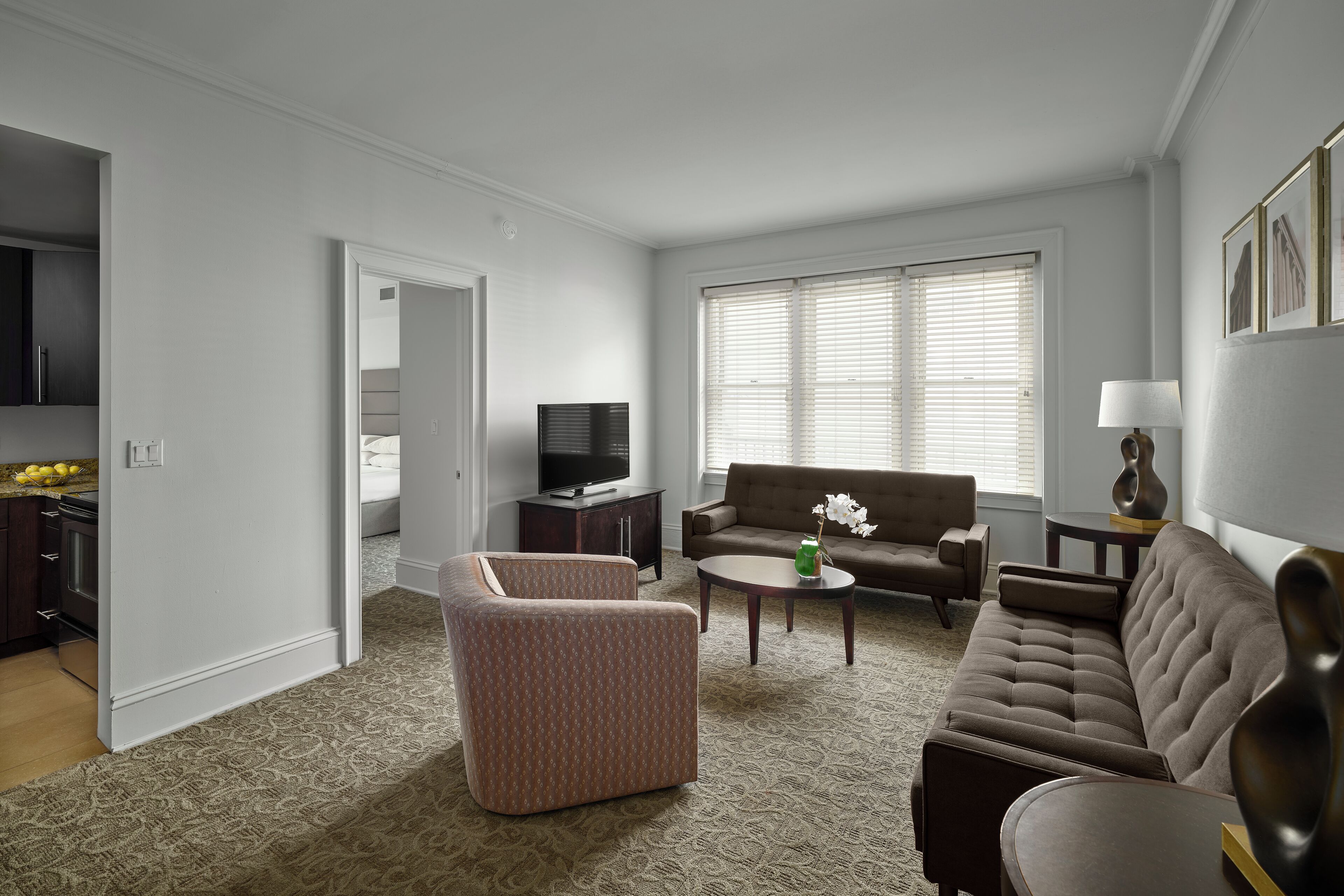 A living room with a sofa, armchair, and coffee table. There is a television and a lamp on a side table.