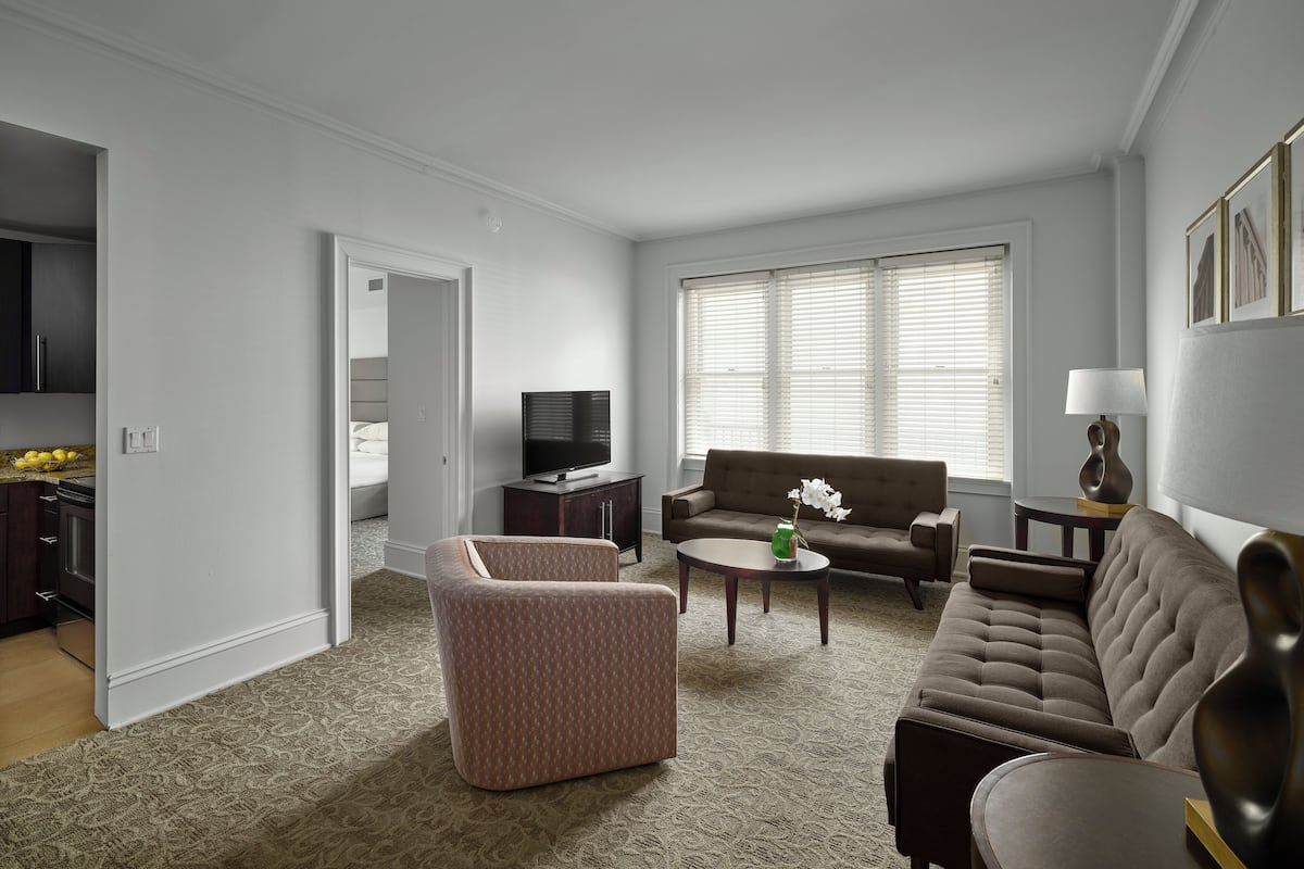 A living room with a sofa, armchair, and coffee table. There is a television and a lamp on a side table.