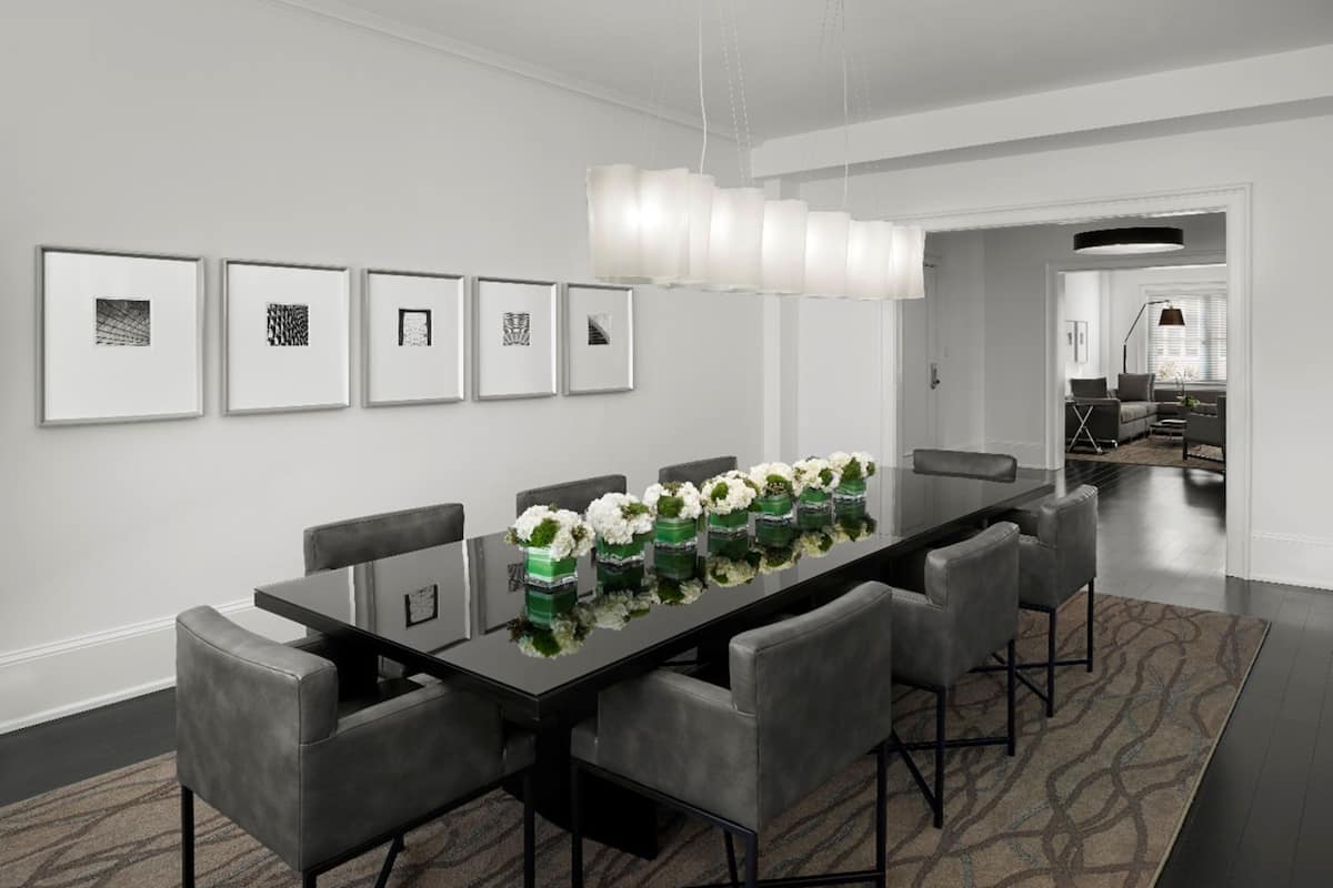 A modern dining area with a long table, six chairs, and a chandelier.