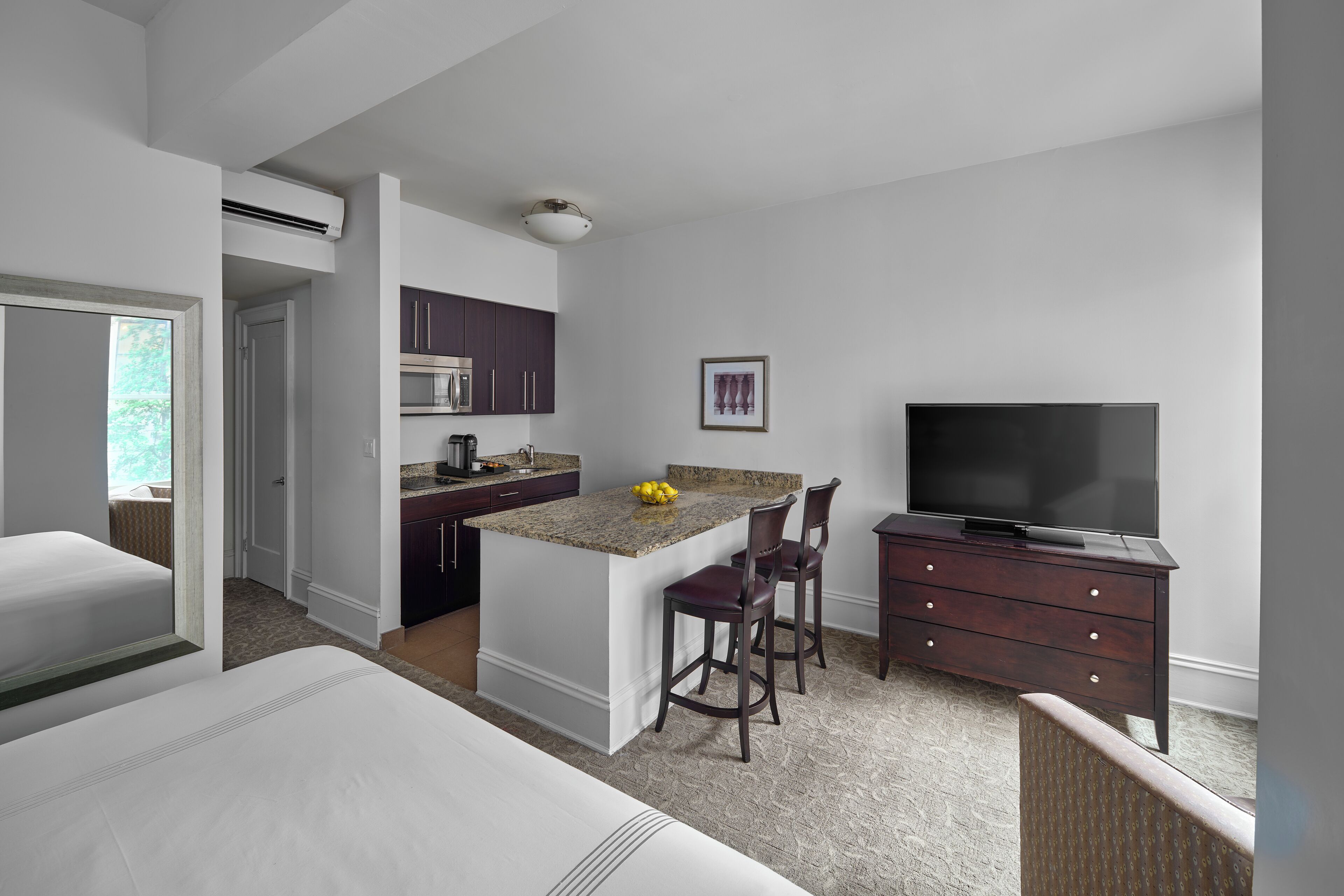 A modern hotel room with a separate kitchen area, a dining space, a TV, and a large bed.